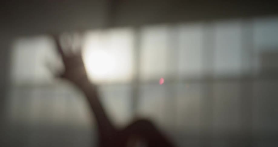 A dancer reaches and stretches their arms in front of a sunny window in a dance studio