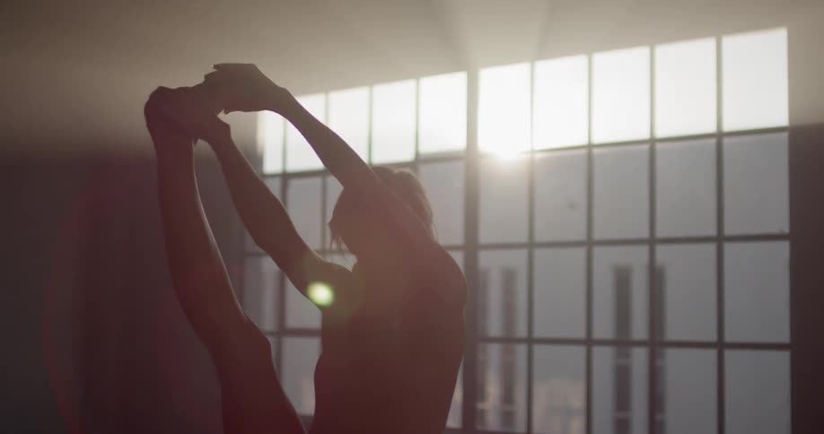 A ballerina practicing in front of a large window in a dimly lit room