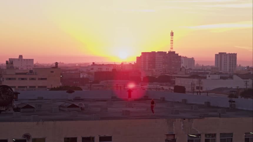 A person dances on a building rooftop in a city at sunset