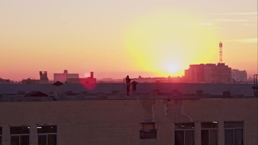 A woman dancing on a rooftop at sunset