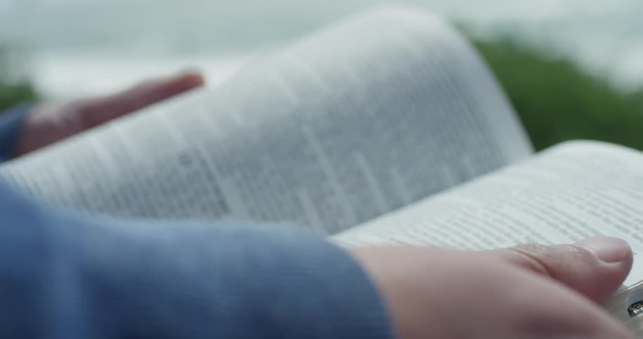 A male with an open book in his hands outside in the wind