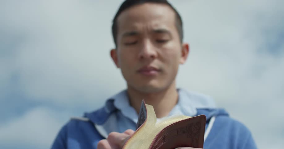 An asian man reads a book that has a red cover