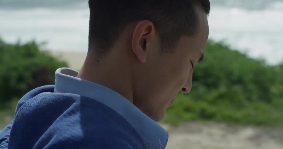 A young man stands on a beach with his eyes closed