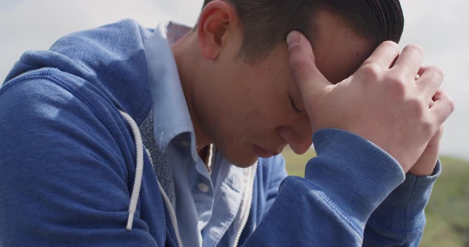 A sad man rests his head in his hands outside on a breezy day
