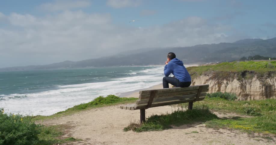 A man sitting on the back of a bench overlooking the coastline