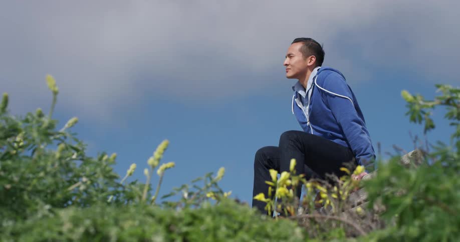 Young man sitting a top some lumber gazes into the horizon as the vegetation sways in the wind