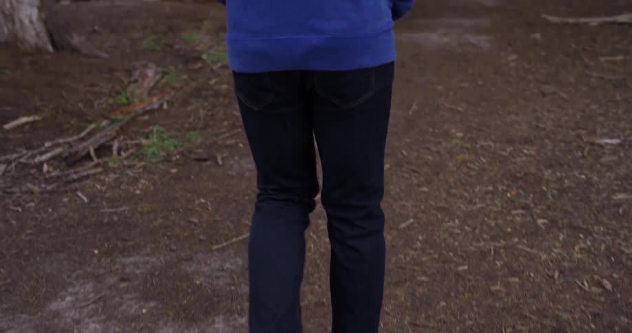 A person in jeans and a blue jacket walks on a path through the woods