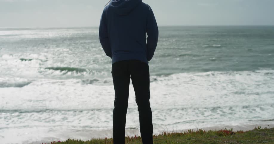 A man stands alone on a beach overlooking an ocean