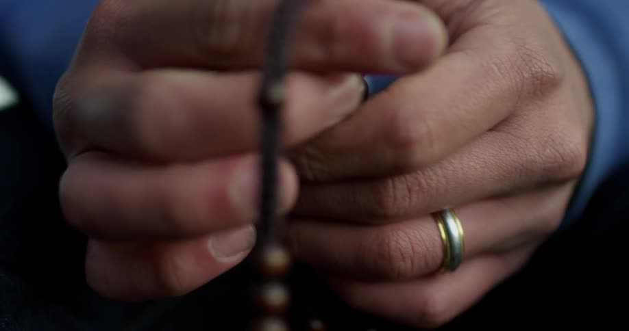 A man holds a cross attached to prayer beads