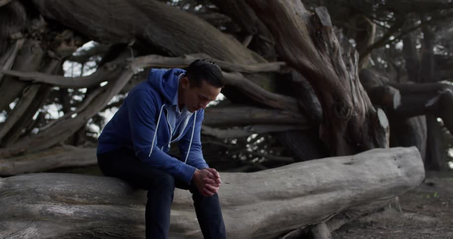 A man sits alone on a piece of driftwood while thinking