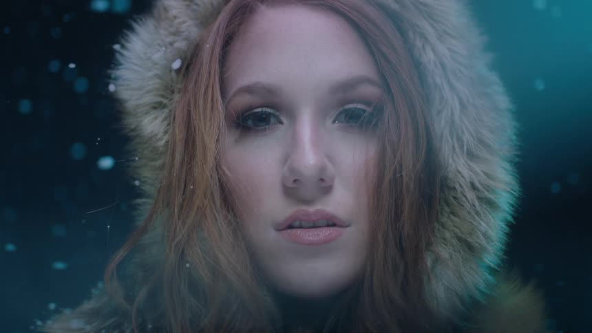 The face of a young woman in a hooded winter coat while snow falls