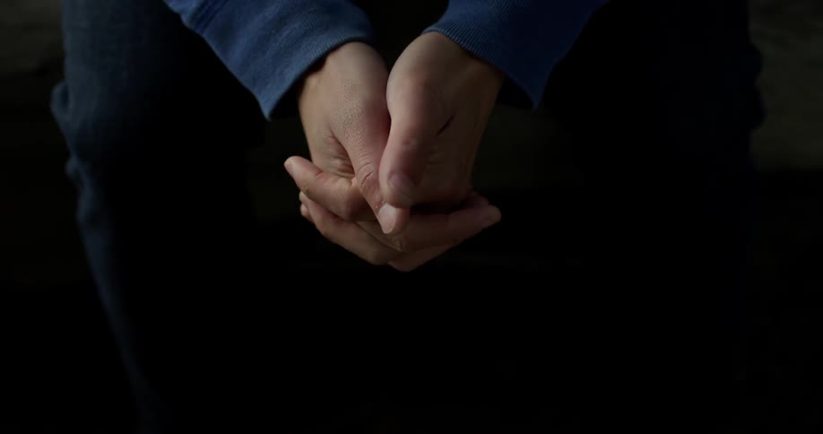 A man sits and clasps his hands together
