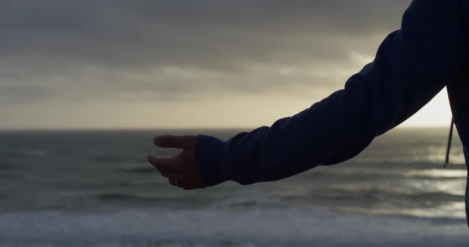 A man holds out his arm while standing on a beach at sunset