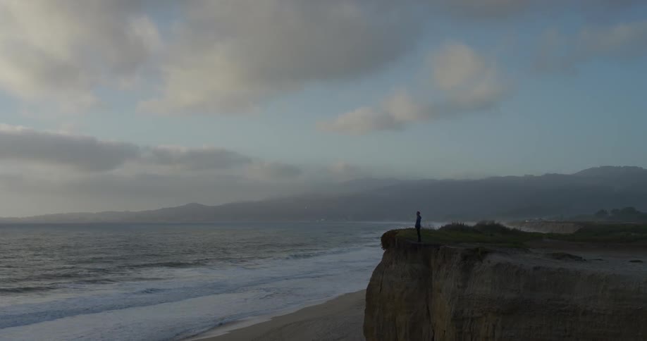 A person standing on a cliff overlooking the beach