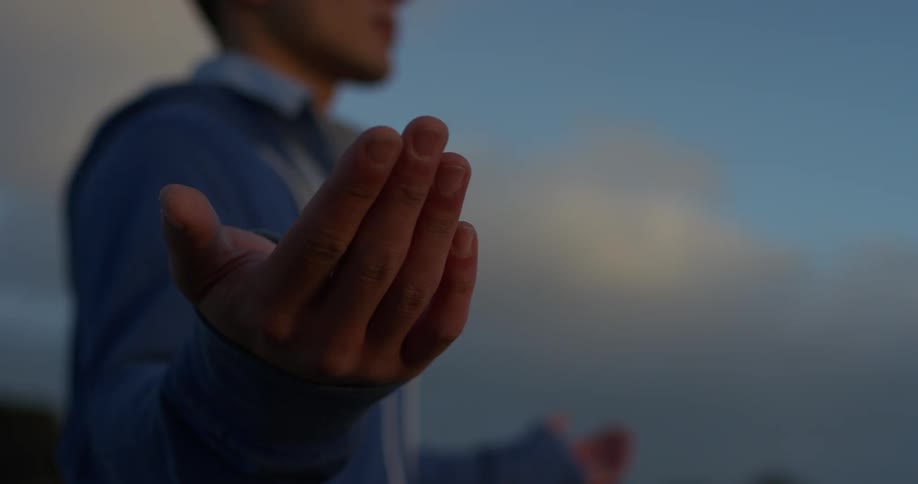 A man standing outside with his hands stretched out praying