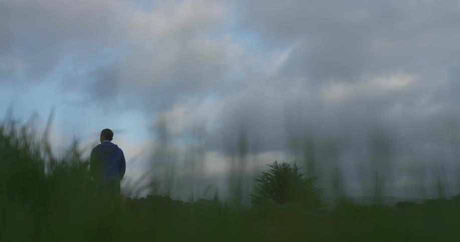 A man is walking through a field with his hands in his pockets on a cloudy day