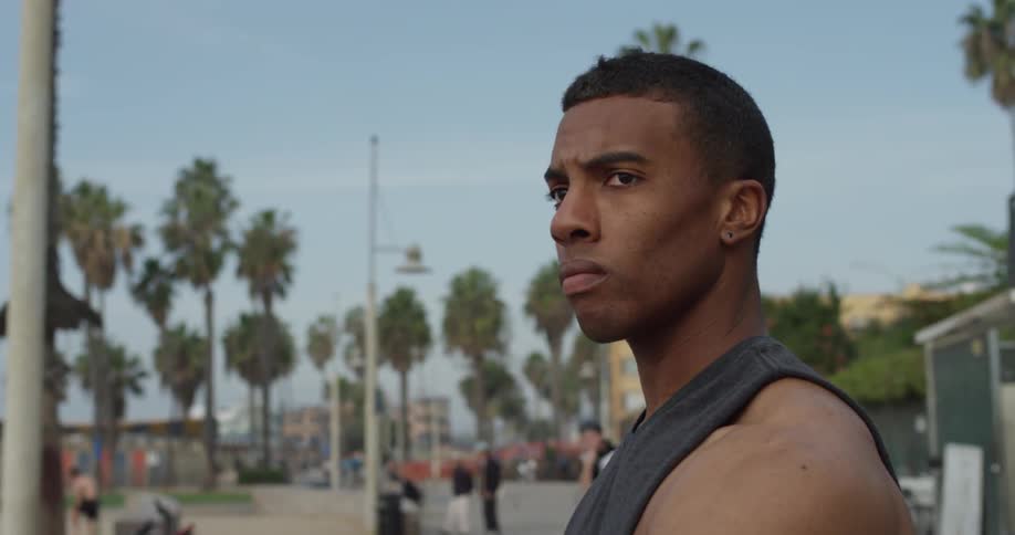 A male in a vest looks left and then down on a busy street under a clear blue sky