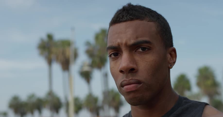 A man standing outside staring with palm trees in the background