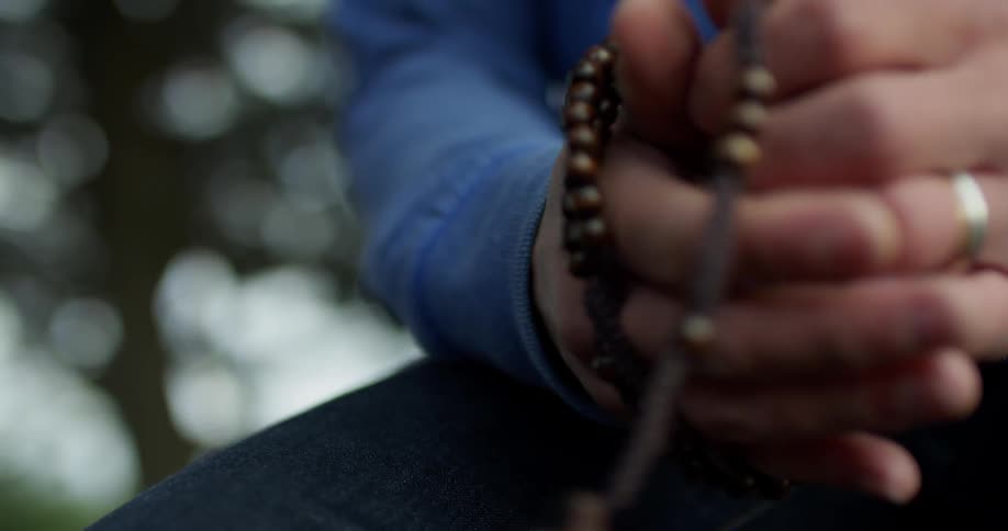 A man wraps a beaded rosary around his wrist and prays
