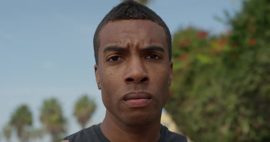 A man standing outside staring with trees and buildings in the background