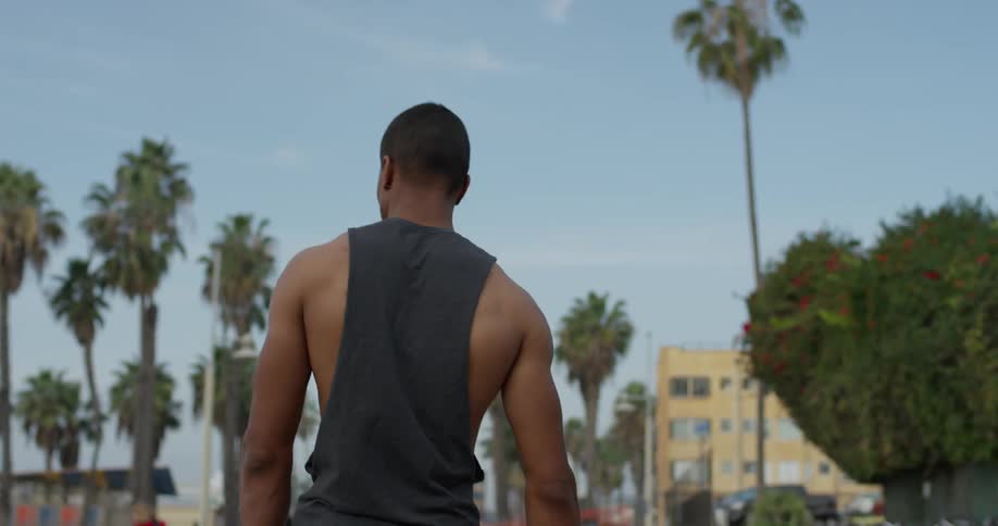 Young black man walks down palm tree lined street