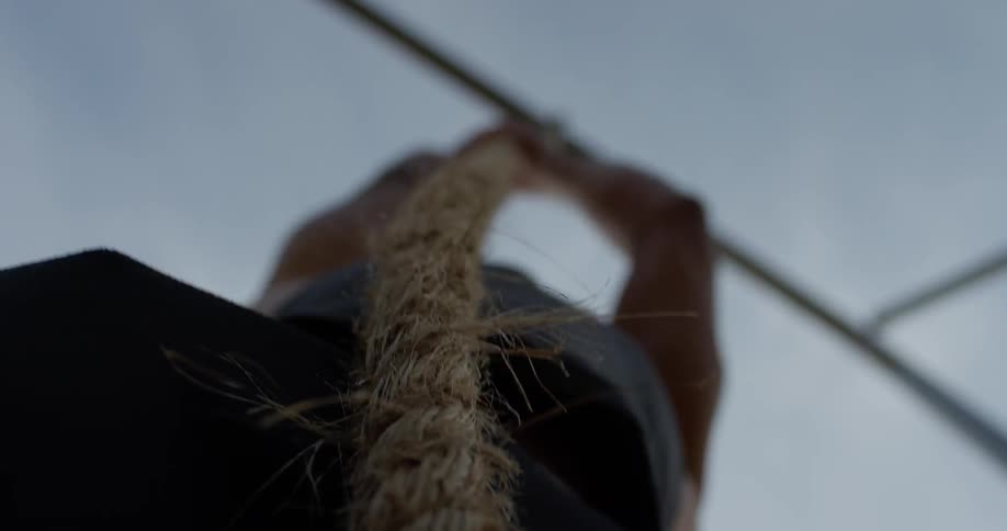 A man in a tank top climbing a rope attached to a pole