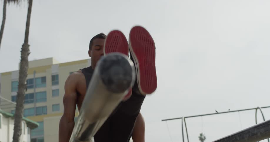 A black man exercises on parallel bars at the beach