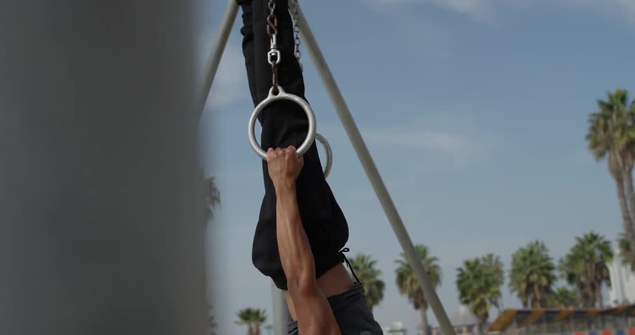 Man trains with gymnastic rings on the beach during daylight