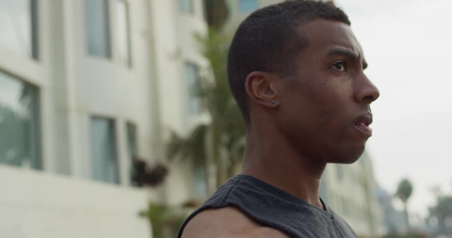 A black man stands outside in the city and looks around at his surroundings