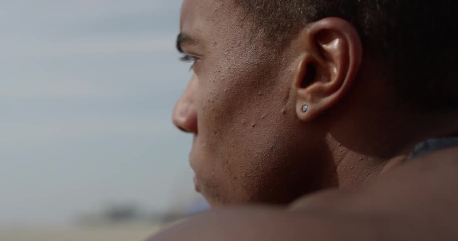 A black man on the beach looks deep in thought