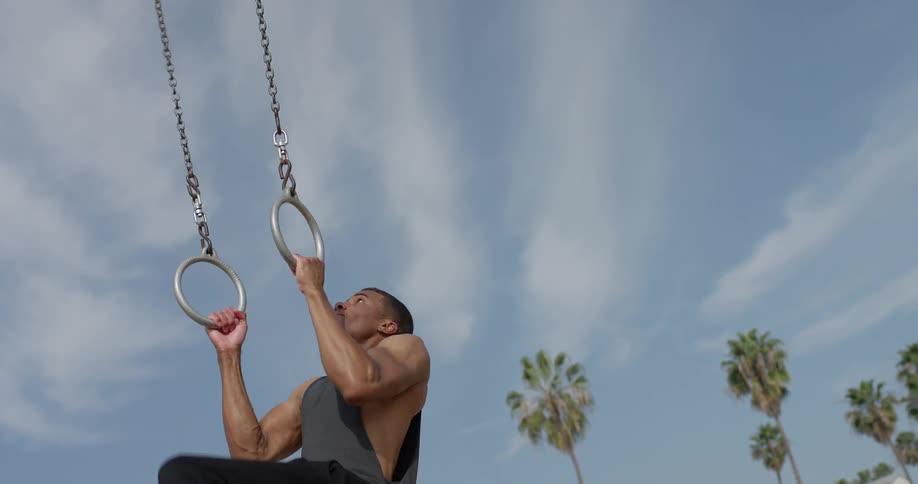 A young black man grabs a steady ring in each hand and pulls himself up until he is hanging upside down