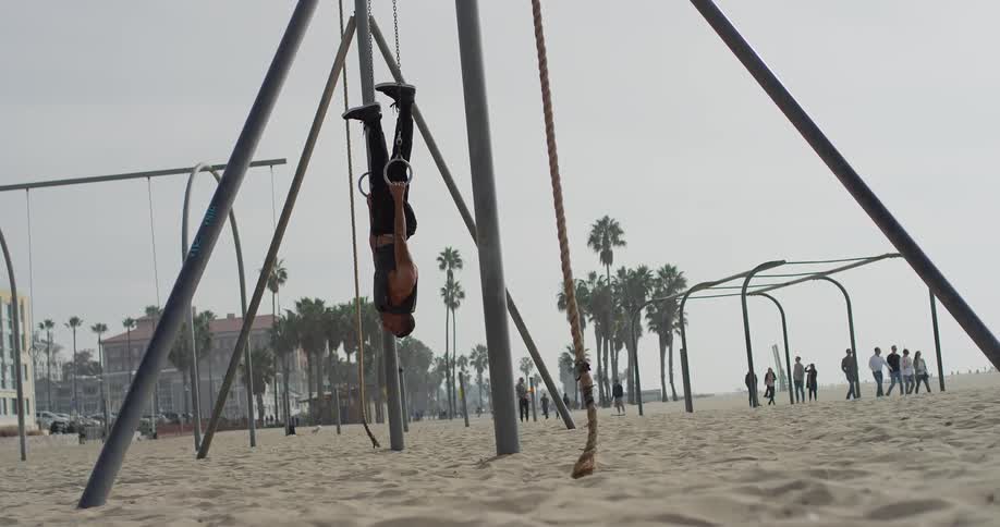 A young man pulls himself up on rings at a playground
