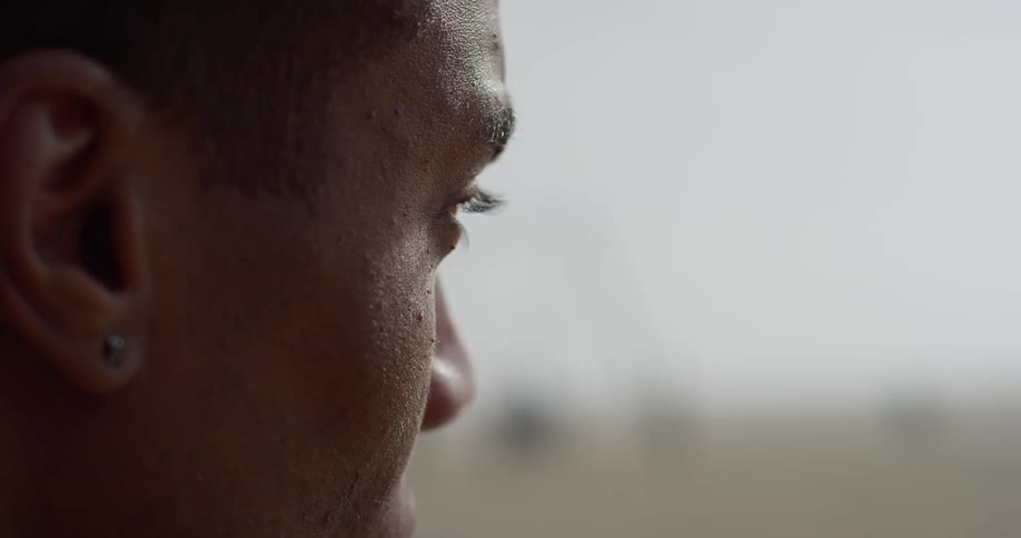 A young black man looks off in to the distance and drinks some water