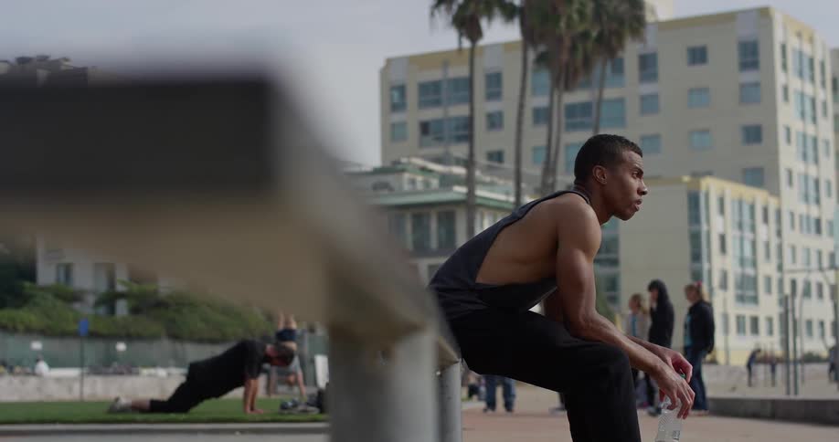 A black man sits on a metal rail at the beach and stares off into the distance