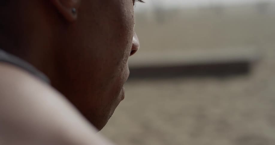 A black man sits on the beach looking upset