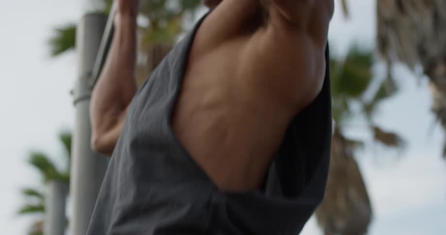 A muscular man in a tank top does pull ups on a beach