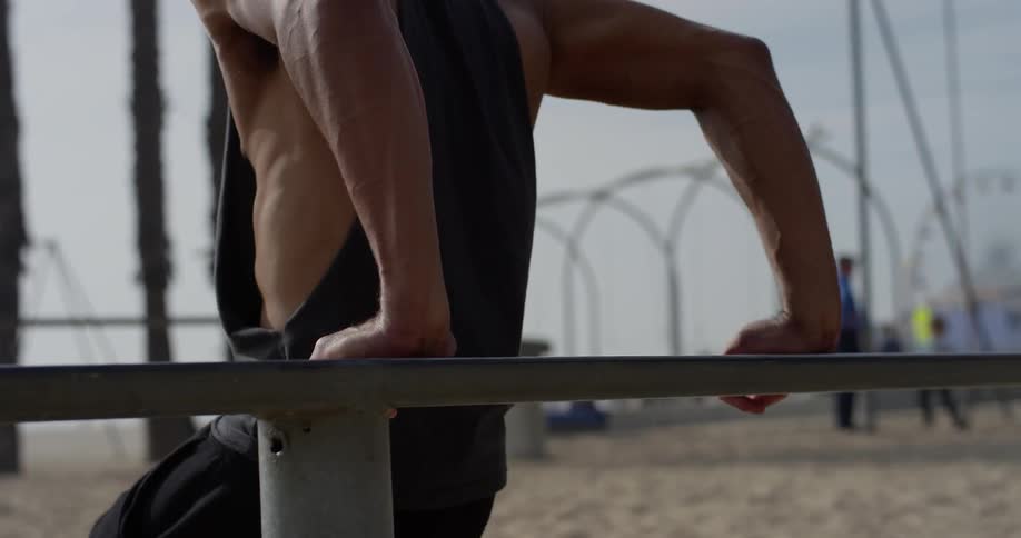 A black man does body lifts on a railing at the beach