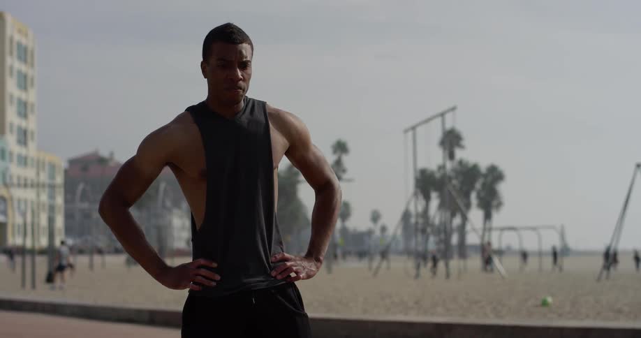 A man stands akimbo with his hands at his waist while standing outside at the beach