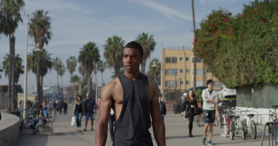 A black man walks down a sidewalk just off of the beach