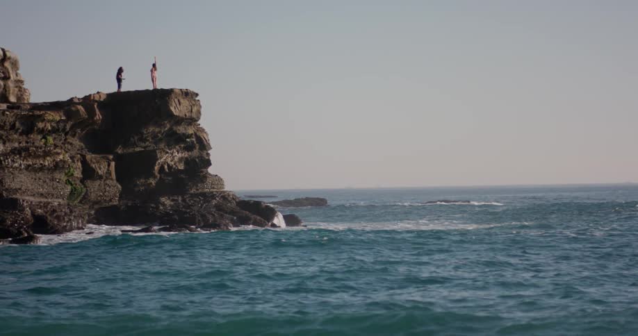 A woman poses for a photographer while on a rocky plateau next to the ocean
