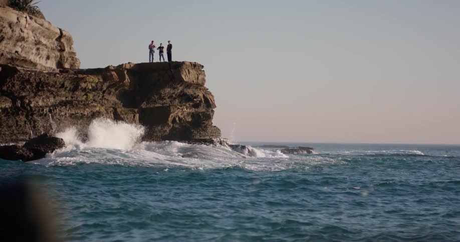 Three people stand at the top of a cliff