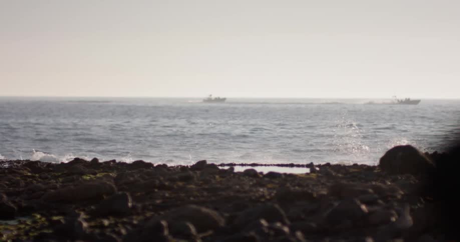 Two water crafts coasting by in the distance near the shoreline