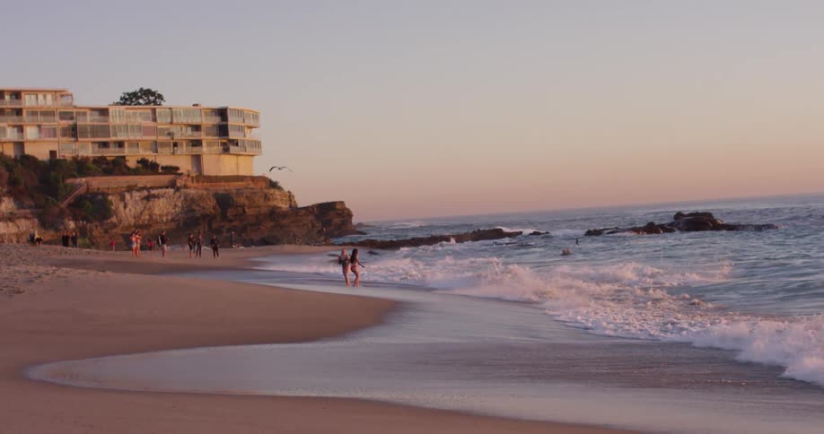 Several people are standing on a sandy beach as large wave crash upon the shore