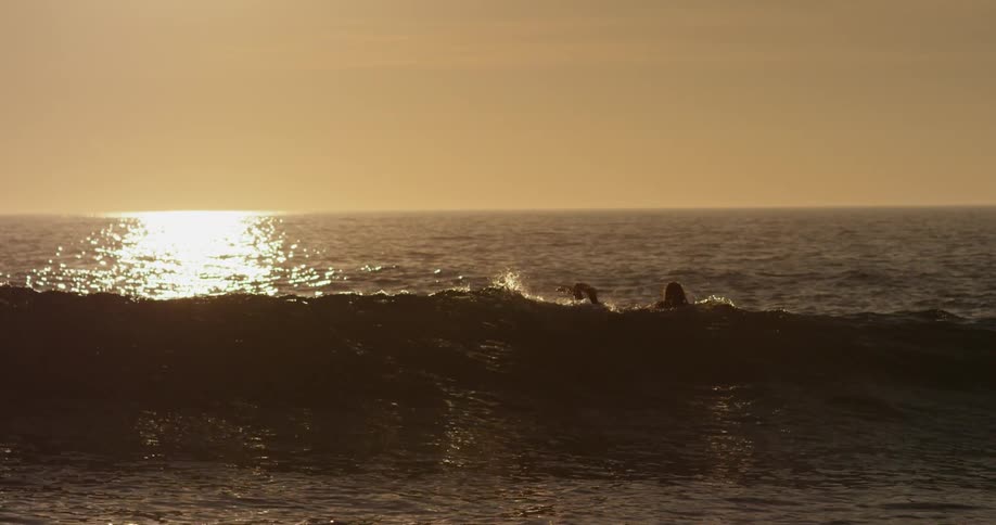 A person laying on a surfboard going over a large wave