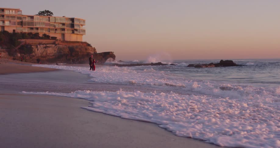 Several people stand on the beach during sunset