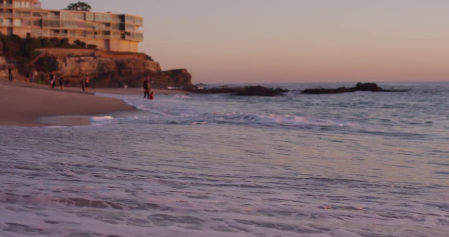 Waves crashing onto a beach with a condo overlooking the coast