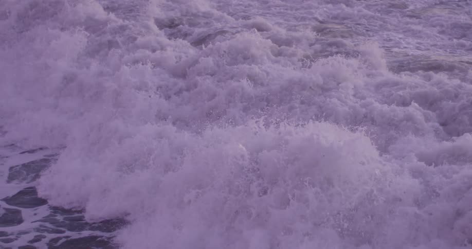 An ocean wave curls and breaks as it comes to shore and a surfer pops out after it covers him