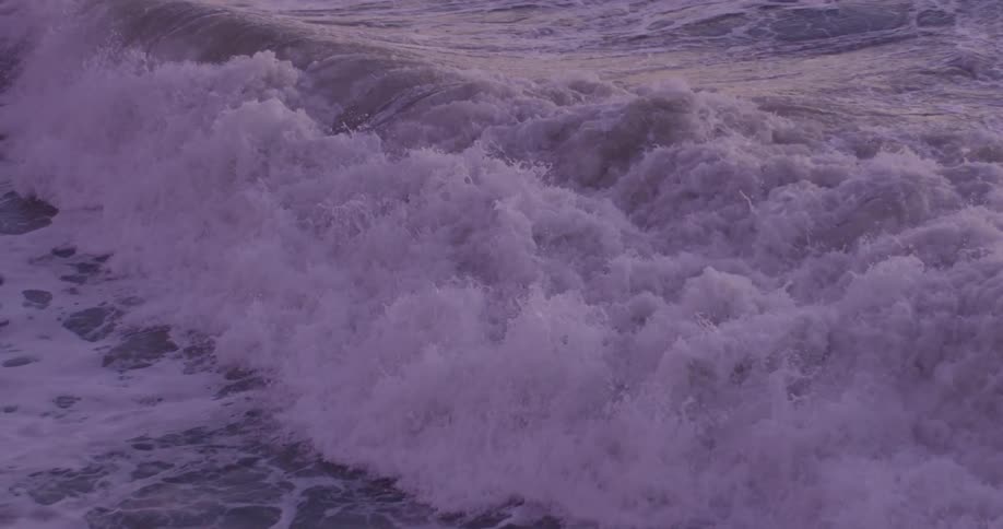 Waves crash against the shore making lots of foam at sunset