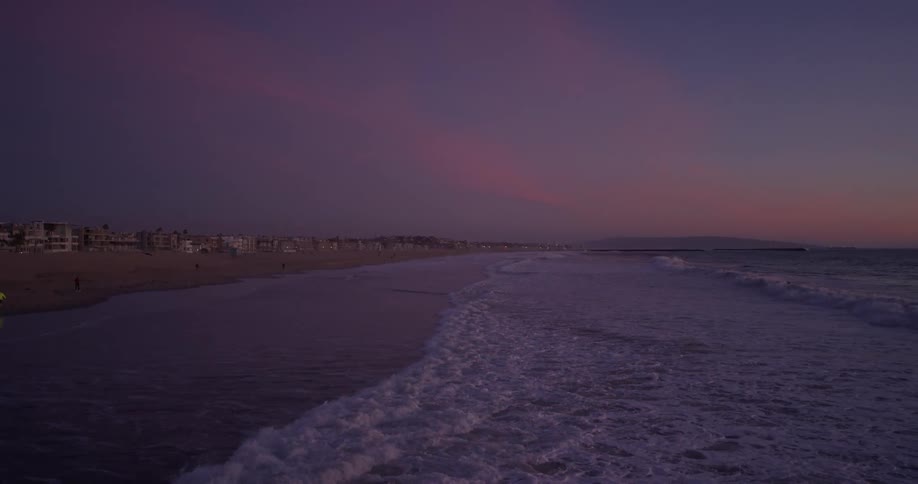 Waves crash against the beach at dusk