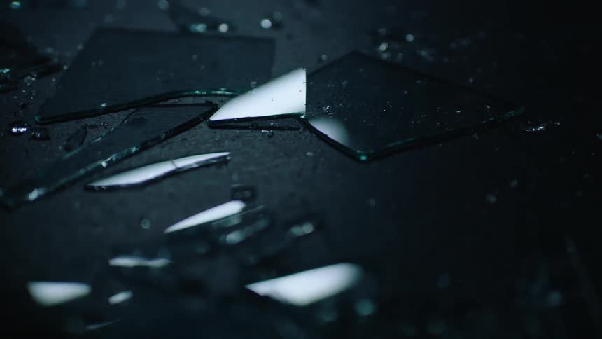 A close view of glass shards on the floor with fluorescent ceiling lights reflecting in the glass